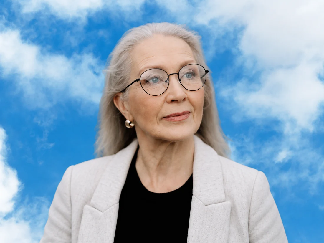 Older woman with gray hair and glasses against a blue sky